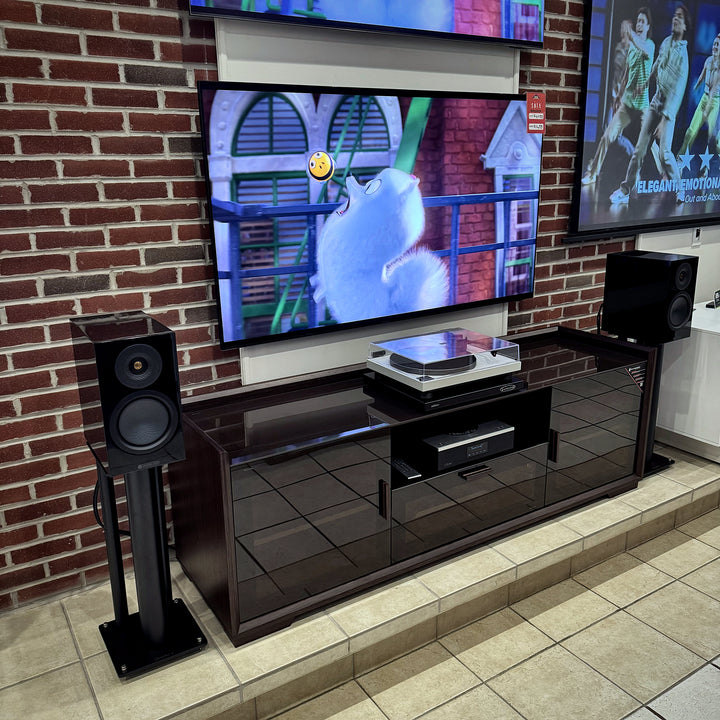Monitor Audio Silver 8G bookshelf speakers in gloss black on stands, flanking a TV and media cabinet with a turntable