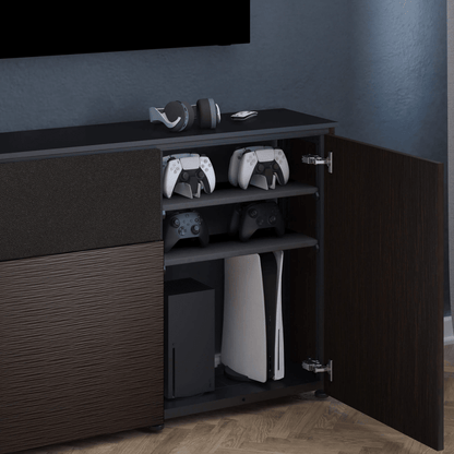 Gaming console and controllers on a dark wooden cabinet against a blue wall.