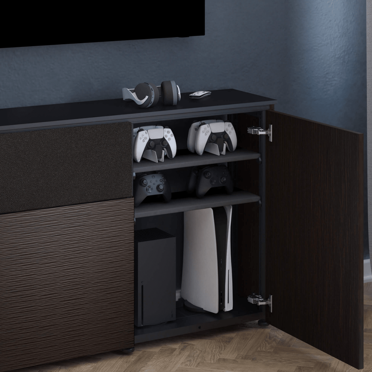 Gaming console and controllers on a dark wooden cabinet against a blue wall.