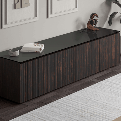 Dark wood entertainment console with black top in a room with framed pictures and a rug.